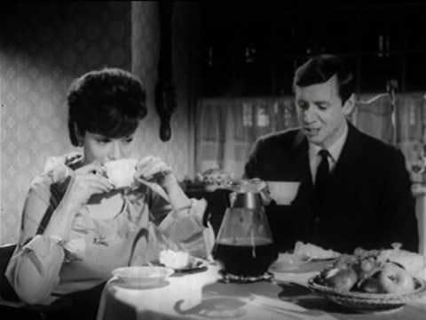 A black and white still from an old Folger's coffee commercial, featuring a man and woman unhappily drinking coffee at a small kitchen table.